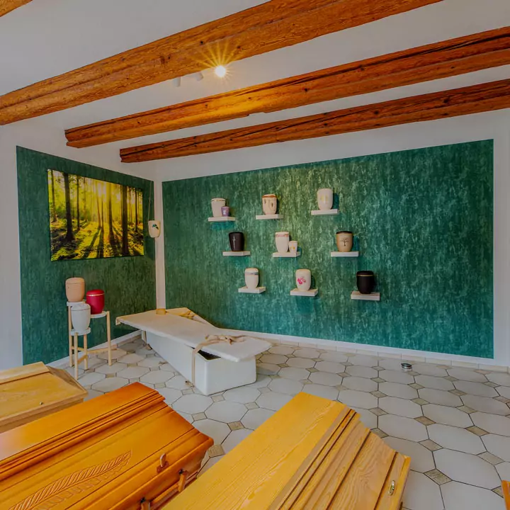 Märtin Bestattungshaus, Bestatter in Ditzingen, Innenansicht des Ausstellungsraums für Särge und Urnen im Standort Ditzingen. Mehrere Särge stehen im Raum und an der grünen Wand sind Regale mit verschiedenen Urnen.